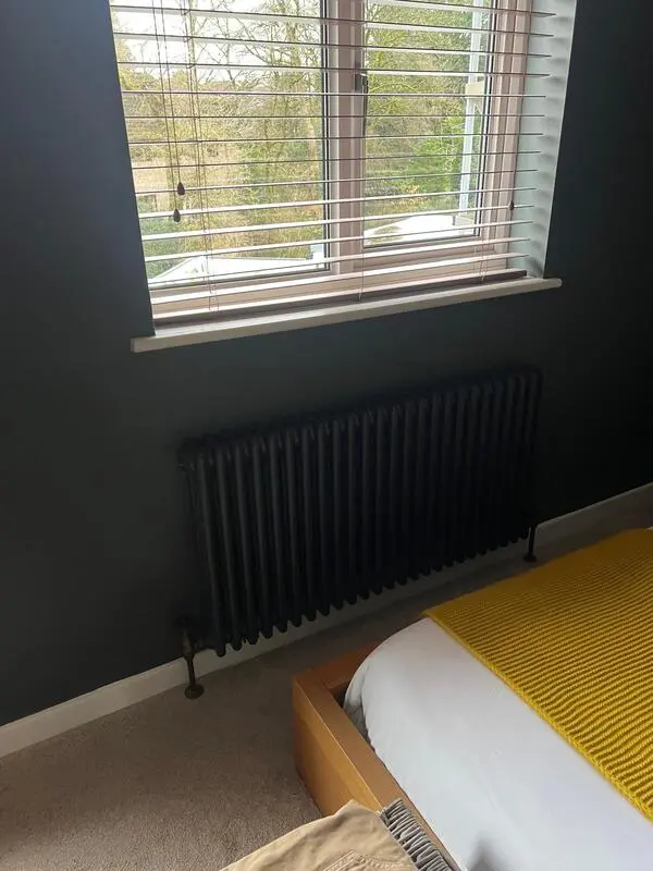 Column radiator installed beneath bedroom window in dark finish